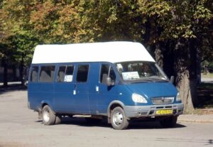 Синя маршрутка з білим дахом стоїть на дорозі, на табло видно номер 5.