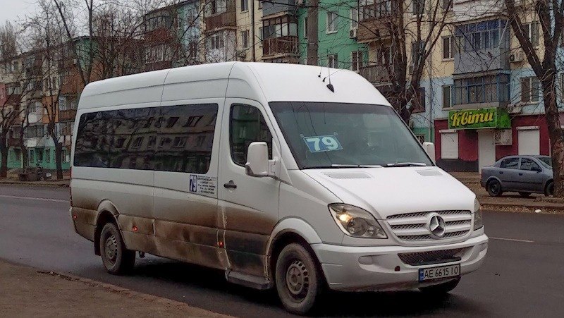 Білий мікроавтобус Mercedes-Benz з номером маршруту 79 на лобовому склі їде дорогою повз житлові будинки.