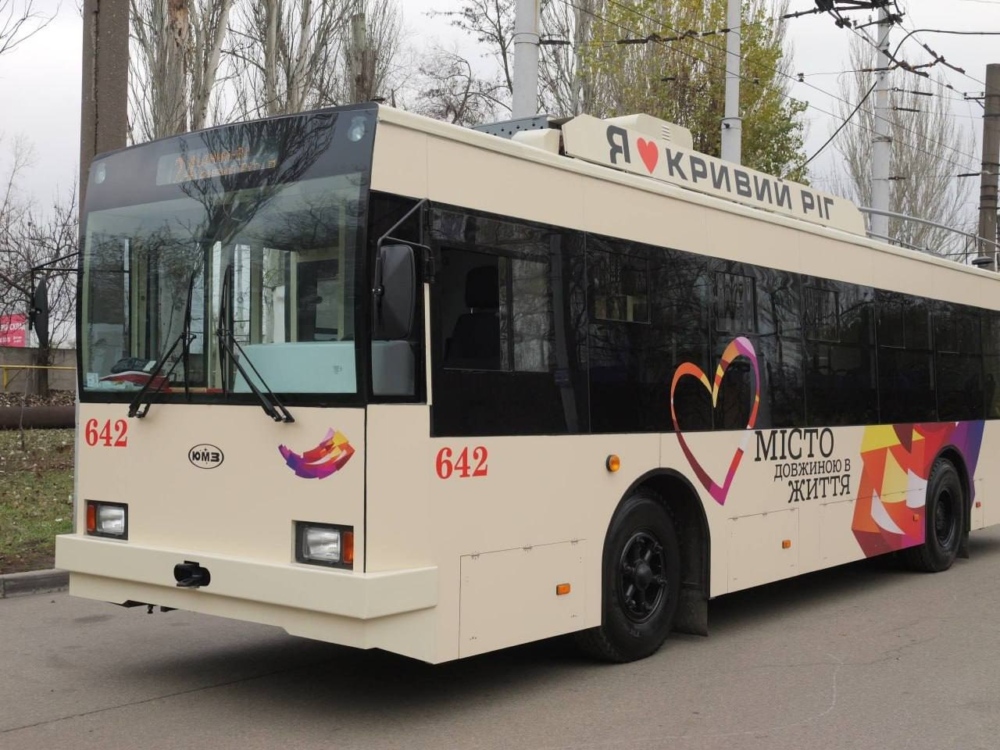 Тролейбус з написом "Я люблю Кривий Ріг" та "МІСТО ДОВЖИНОЮ В ЖИТТЯ" на борту, стоїть на вулиці.